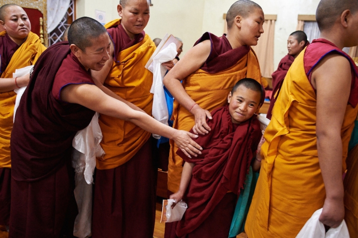 A young Tibetan Buddhist nun being coached by her sister nuns in how to offer respect to the nunnery leaders