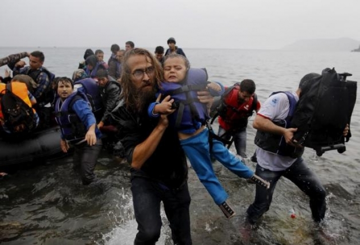 A volunteer carries a Syrian refugee child off an overcrowded dinghy to a beach on the Greek island of Lesbos in September 2015. Photo by Yannis Behrakis. From reuters.com