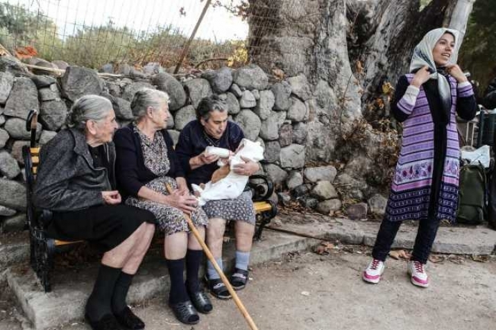 Emilia Kamvisi, third from left, feeding the baby of a Syrian refugee. Photo by Lefteris Partsalis. From neoskosmos.com