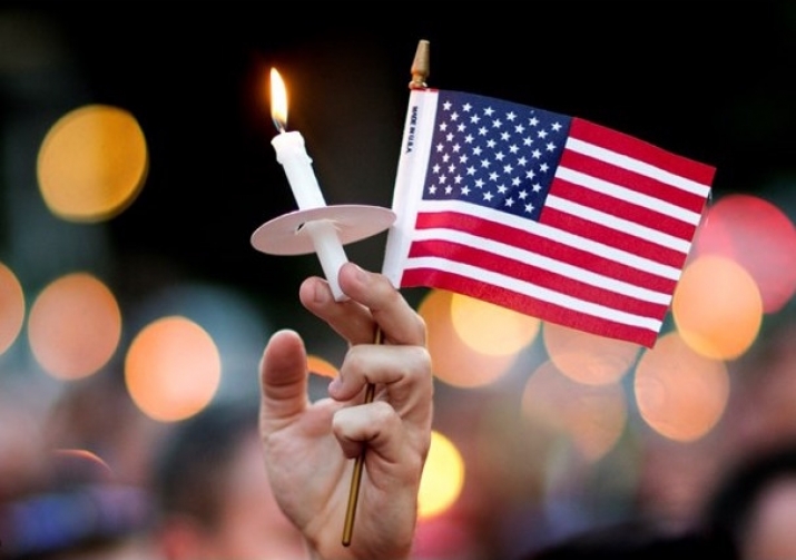 A mourner holds up an American flag and candle during a vigil for the vicitms of the shooting. From en.radiovaticana.va