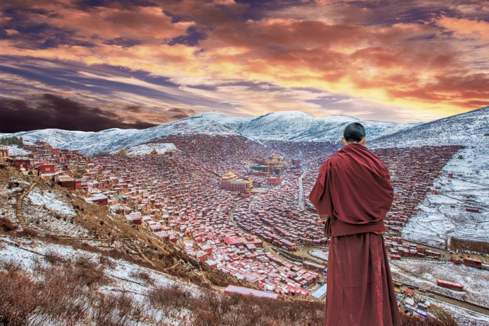 A monk stands on a hillside overlooking Larung Gar Buddhist Academy. From imagesforworld.com
