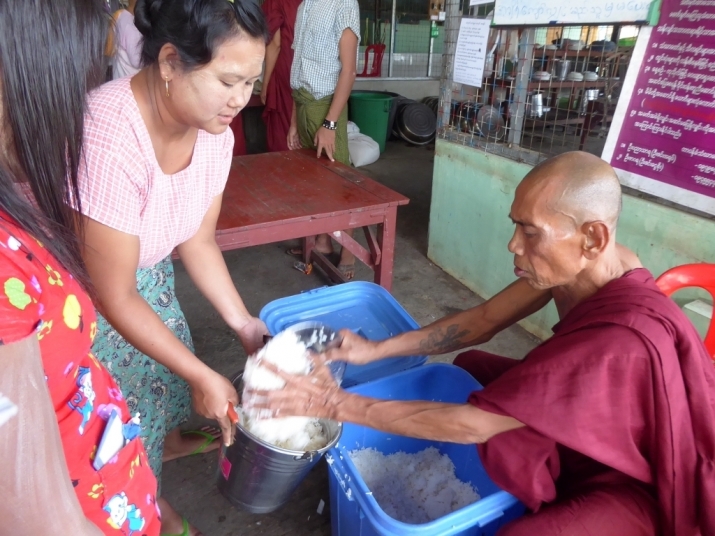 A monk fills a bucket of rice for distribution