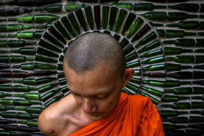 A monk in front of a glass bottle wall at Wat Charok Padang, Malaysia. Photo by Seth Akmal. From themalaysianinsight.com