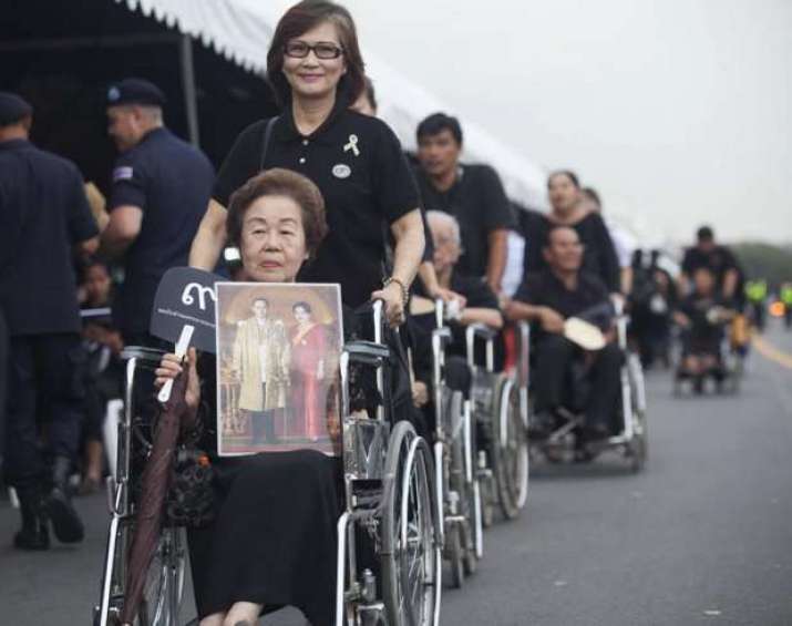 Elderly people in wheelchairs are assisted by family members as they wait their turn in line. From bangkokpost.com