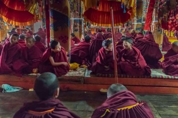 2018. Wu Village Lower Monastery. Young monks chat during a long ceremony. I had stood in the same place long enough for them to forget about me and start chatting among themselves. I took the shot from my waist instead of raising the camera to my eye. Near the center of the photo is the pole that supports a circular banner used by the monks for parades in ceremonies—annoying from a photographer’s point of view, but these photos are supposed to be real, not photoshopped, so I didn’t remove it.